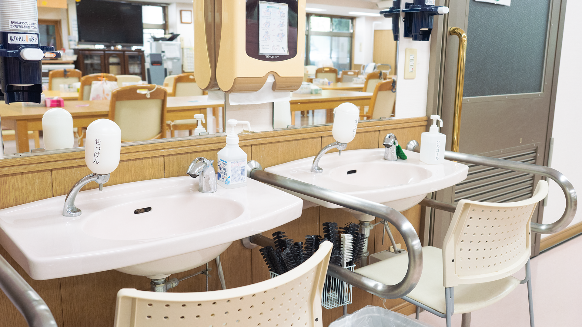 二連の手すり付き洗面台と消毒ディスペンサーのある洗面コーナー