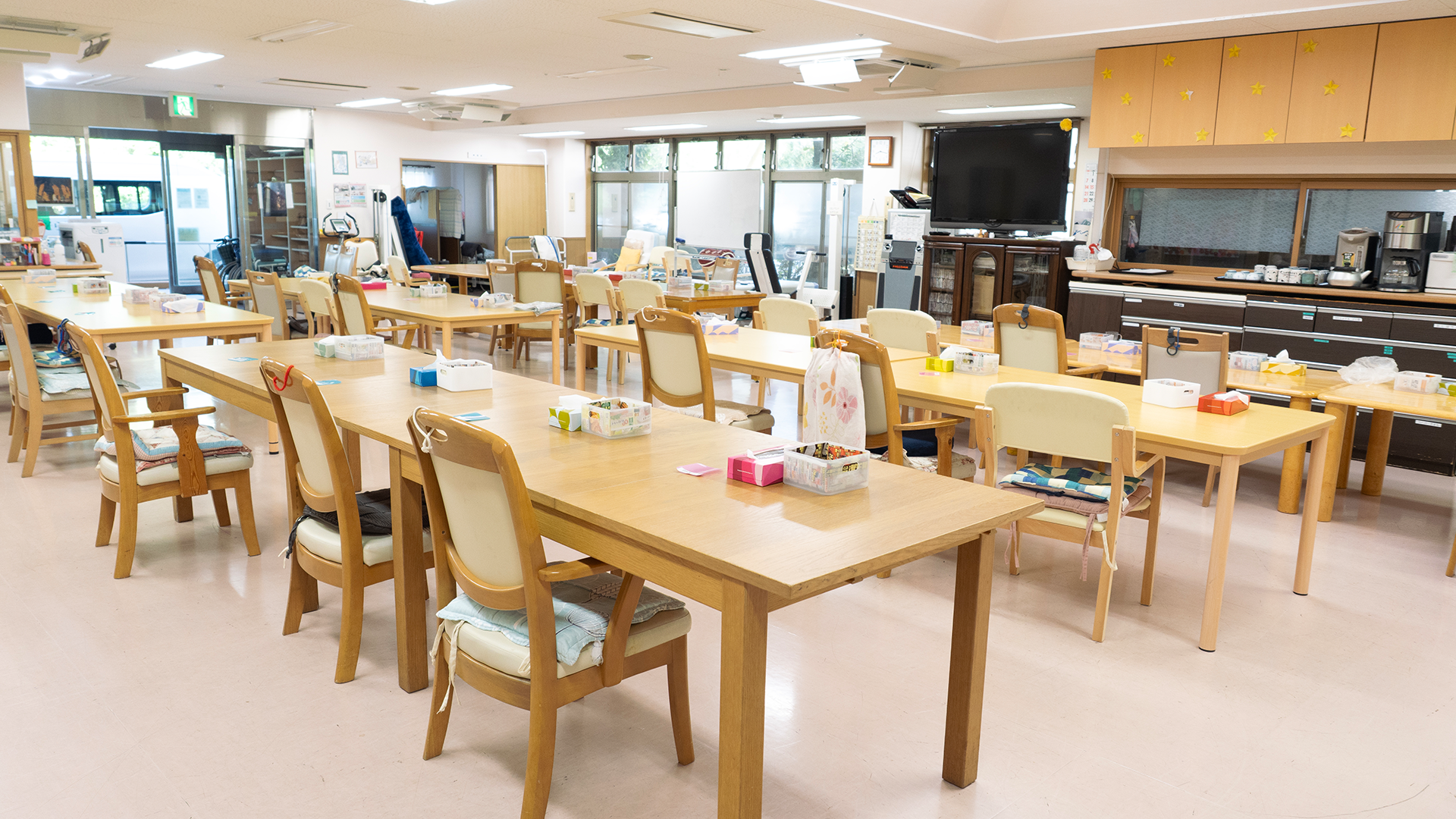 デイルームの全景（テーブル・椅子が整然と並ぶ明るいフロア）