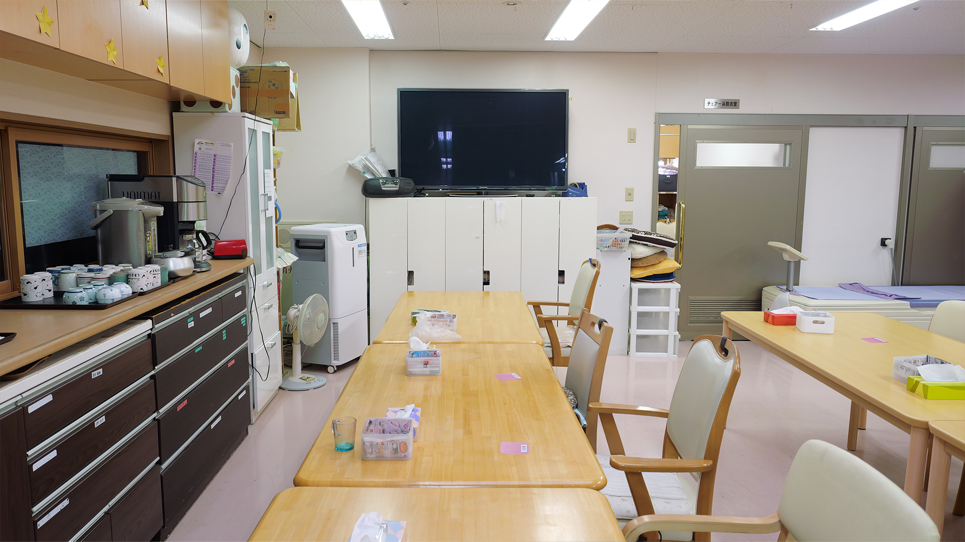 明るいデイルーム全景（テーブル・椅子・テレビ・配茶スペース）